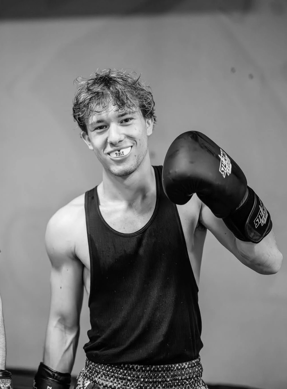 Aleks Szulc smiling with a mouthguard and boxing glove raised
